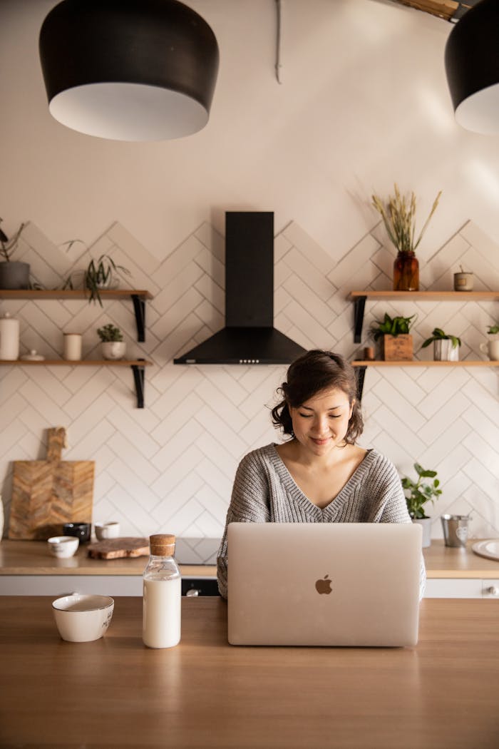 core-values Young female student in gray sweater sitting at wooden desk with laptop and bottle of milk near white bowl during distance education at home