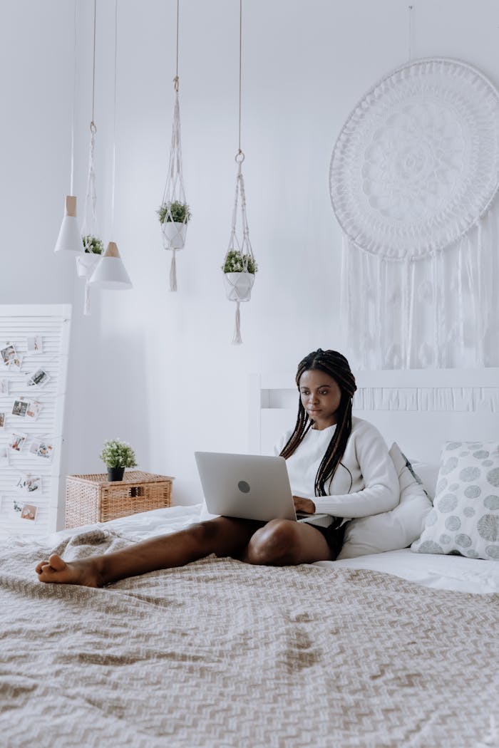 Woman enjoys online activities on laptop in a cozy, stylish bedroom.
